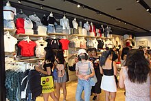 A store with clothes on the wall, full of mostly young women customers