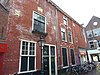 Pand met vlakke gevel met sobere gootlijst, zijgevel Haarlemmerstraat 142. Gevelsteen Schaap met twee wolven. Twee cartouches met jaartal.