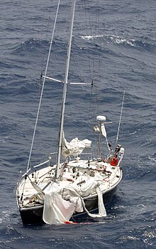 Das Bild zeigt ein Segelboot mit zerfetzten Segeln, das außerdem sehr tief im Wasser liegt, weil offenbar schon Wasser eingedrungen ist.