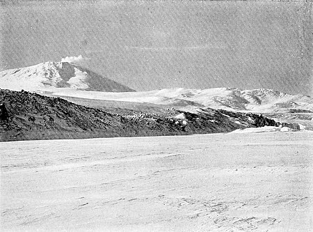 Photograph of a volcano fronted by a steep coast across sea ice