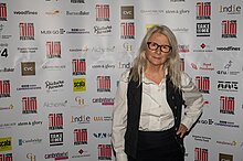 stylish woman with long grey hair infront of a cambridge film festival sponsors board