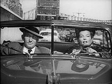 Screenshot of Hepburn and Spencer Tracy sat in an open-top car in mid-conversation. He looks unimpressed.