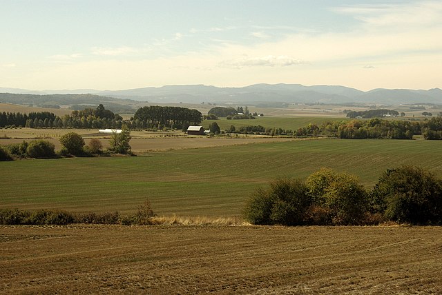 Farm fields spread into the distance, where a barn and far-off mountains can be seen