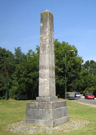 Colonne de pierre élevée sur une base carrée dans le gazon et à proximité d'une route.