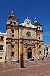 Facade of a yellow stone church with two towers. Above the main entrance there is a human sculpture and higher up a clock.