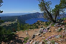 Vue plongeante depuis un sentier sur une partie de la caldeira et son lac, avec des installations touristiques au second plan à gauche.