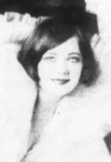 A young white woman with a dark bobbed hair in a side-part, wearing a white fur wrap