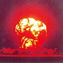 A mushroom cloud fading from deep red on the edges to white on the inside all surrounded by a circular red glow in a dark purple sky