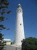 Wadjemup Lighthouse, a whitewashed stone structure seen against a blue sky, with small buildings at the base