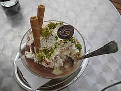 Helado con diferentes decoraciones: barquillos, pistacho en grano y un botón de chocolate con el logo de la marca.