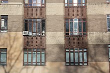 Two bays of bow windows on the second and third stories are visible here. Each window is divided horizontally and vertically by mullions. The windows on different floors are separated horizontally by rust-colored spandrels. Windows on the same floor are separated vertically by panels of darker-brown brick. Below the second-story windows is the stone base. Central Park West Mar 2022 15.jpg