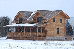 Two-story log house in winter, with large porch and dormer roof