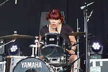 A female drummer, Lori Barbero, seated behind a drumkit, in a performance setting.