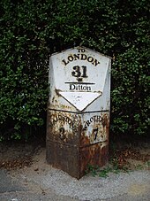 A photograph showing a small monument at the roadside. The bottom of the white cast-iron monument is v-shaped towards the road. The right-hand side reads 'WROTHAM 7' and the left reads 'MAIDSTONE 3'. There is rust damage to its base. On the head of the monument, parallel to the road, the legend, in black-painted relief, reads 'To LONDON 31'