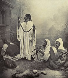 حُواةٌ مغاربة في طنجة في أواخر القرن التاسع عشر أو أوائل القرن العشرين، أحدهم يُمسكُ الحيَّة، والثاني ينفخُ في المزمار، بينما الثالث والرابع ينقران على دُفوف