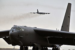 B-52H Stratofortress на 5-то бомбено крило седи на полетната линия, когато друг B-52H излита от Minot AFB.