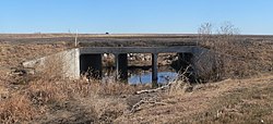 Road crossing rectangular concrete culvert, divided into three square sections; water in bottom