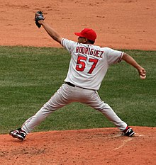 빨간색 모자와 회색 유니폼을 입고 마운드 위에서 오른손으로 공을 던지려는 자세를 취하고 있는 남자이다.