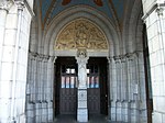 Le porche et l'entrée. Sur le pilier centrale est placée une statue de Notre-Dame de Lourdes. Sur le tympan du portail sont représentés le Christ pantocrator et le tétramorphe