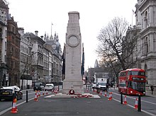 A stone monument in the centre of a street with traffic passing