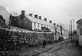 Black and white photograph of the tram road next to a wall and a row of houses