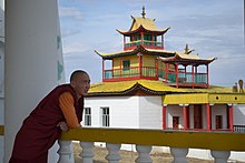 Buddhistický mnich na Sibiři v šatech opírajících se o zábradlí při pohledu na chrám