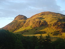 Una montaña cubierta irregularmente por vegetación, cerca de la puesta de Sol.