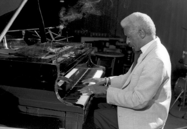un homme noir-américain aux cheveux blancs est assis au piano