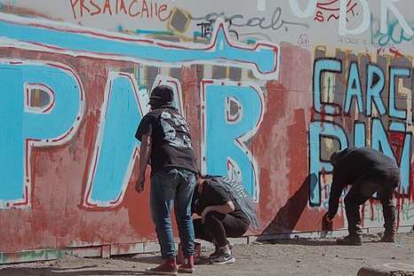 Muralistas en aniversario del 18 de octubre pintando sobre reja instalada en Plaza Baquedano