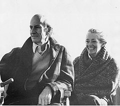 Bald man in overcoat next to woman wrapped in a blanket