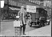 A man dressed as Santa Claus fundraising for Volunteers of America on the sidewalk of street in Chicago, Illinois, in 1902. He is wearing a mask with a beard attached. Chicago Santa Claus 1902.jpg