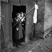 Photo noir et blanc montrant deux adolescents aux visages inquiets et levant les mains dans l'encadrement d'une porte. Une perche portant un tissu blanc dépasse de la porte.
