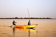 Brillamment éclairée par le soleil couchant une barque voguant sur le lac et portant deux hommes semble se transformer en or.