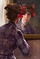 Oil painting of a woman in a high necked, long sleeved dress looking at herself in the mirror. Her hair is in a bun and she wears a brown hat with red flowers on the right side.