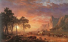 landscape painting with covered wagons, men on horses, mountains with cliffs on the right and a sunrise seen through the trees on the left