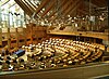 A modern photograph of a large chamber with many desks and chairs arranged in a semicircle