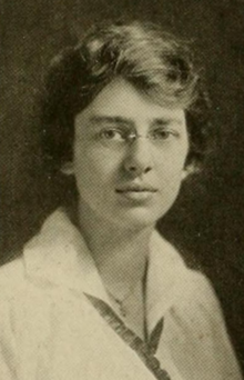 A young white woman wearing glasses and a white collared blouse; she has dark hair.