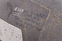 Sur le bitume, un graffiti "Je suis Alain Soral" réalisé avec un pochoir. Le nom d'Alain Soral est barré au marqueur par une personne ayant écrit à côté "Pas de nazi dans nos quartiers ! Pas de quartier pour les nazis !".