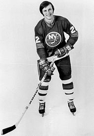 Mike Bossy in a hockey jersey, wearing gloves and holding a hockey stick, with ice skates on