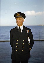 Mack standing on the deck of a ship with the sea and sky behind him.