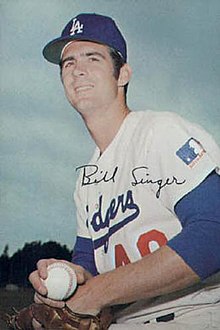 A man in a white baseball uniform and blue undersleeves and cap