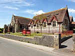 Picture of the Wesley Methodist church in Front Street, Churchill, taken from the opposite side (south) of the road. The church is shown with red painted window ledges and the cemetery surrounded by red railings