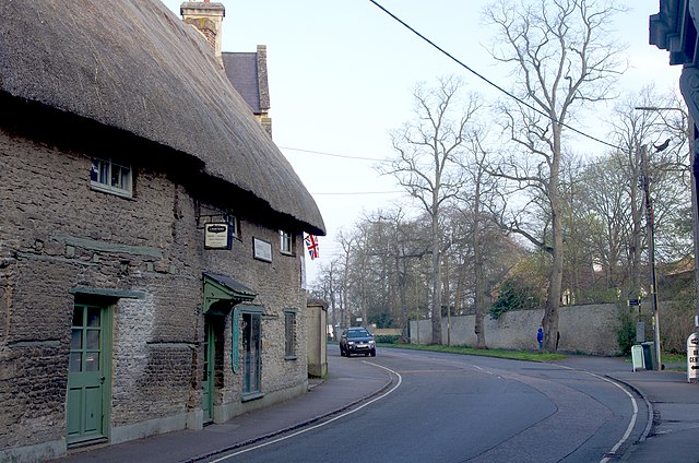 Thatched stone building in quiet, tree-lined, street