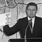 Photographie en noir et blanc d'un homme en costume présentant un rapport.