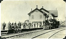 Une gare avec des passagers sur le quai et une locomotive à vapeur.