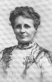 Older white woman, lace-trimmed dress, high collar, hair in an updo.