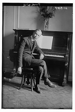 Photographie en noir et blanc d'un homme assis devant un piano droit