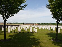 Cemetery with irregularly placed gravestones and the Cross of Sacrifice in the background, framed by two trees