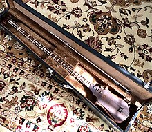 The sato is inside an open cloth-lined hard case, and the bow (similar to a violin bow) is clipped inside the lid. The case rests on a central Asian carpet.