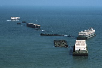 The remains of the harbour off Arromanches in 1990 Arromanches Mulberry-Harbour Phoenix-Elements 1 90.jpg
